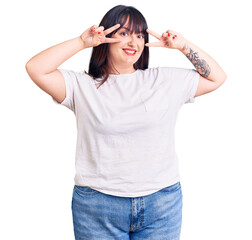 Sticker - Young plus size woman wearing casual clothes doing peace symbol with fingers over face, smiling cheerful showing victory