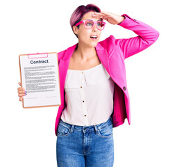 Canvas Print - Young beautiful woman with pink hair holding clipboard with contract document very happy and smiling looking far away with hand over head. searching concept.