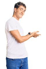 Wall Mural - Young handsome man wearing casual white tshirt inviting to enter smiling natural with open hand