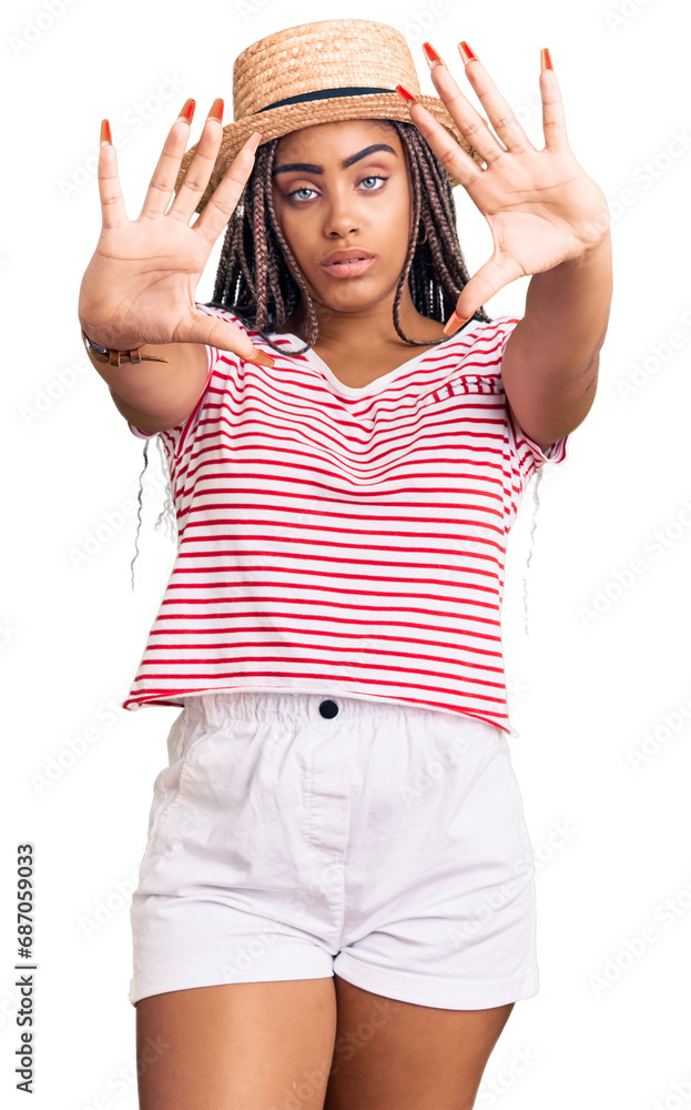 Young african american woman with braids wearing summer hat doing frame using hands palms and fingers, camera perspective