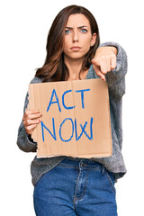 Wall Mural - Young brunette woman holding act now banner pointing with finger to the camera and to you, confident gesture looking serious