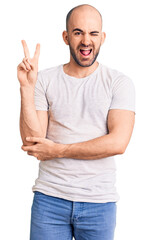 Wall Mural - Young handsome man wearing casual t shirt smiling with happy face winking at the camera doing victory sign. number two.