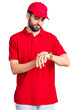 © Krakenimages.com - Young handsome man with beard wearing delivery uniform checking the time on wrist watch, relaxed and confident