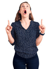 Wall Mural - Young beautiful blonde woman wearing casual shirt amazed and surprised looking up and pointing with fingers and raised arms.