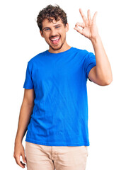 Wall Mural - Young handsome man with curly hair wearing casual clothes smiling positive doing ok sign with hand and fingers. successful expression.