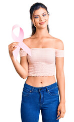 Sticker - Young beautiful woman holding cancer awareness pink ribbon looking positive and happy standing and smiling with a confident smile showing teeth