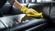 Closeup woman hand in yellow glove cleaning black leather sofa