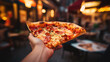Closeup man hand holding slice of pepperoni pizza on blurred cafe background