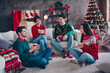 © deagreez - Full body photo of four cheerful friendly people sit sofa carpet floor enjoy hot chocolate communicate decorated house indoors