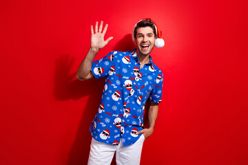 Sticker - Photo of good mood friendly guy wear christmas hat print shirt waving hand to you say hello isolated on vivid red color background