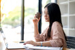 © Wasana - Asian business woman sitting and working in front of a laptop, holding a cup of coffee work independently and relax.