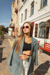 © alones - Fashionable beautiful business girl model with vintage sunglasses in fashion clothes with a blazer walks on a sunny day in the city.