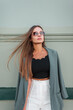 © alones - Beautiful fashionable young woman business lady with vintage sunglasses in a fashion outfit with a blazer stands near a green wall in the city