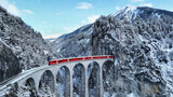 Fototapeta Krajobraz - Snow falling and Train passing through famous mountain in Filisur, Switzerland. Train express in Swiss Alps snow winter scenery.