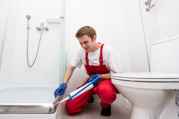 Young man in uniform repairs the shower door in the bathroom. A male repairman repairs the shower cabin.