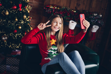 Sticker - Portrait of friendly adorable teenager with blond hair dressed red sweater making selfie on smartphone show v-sign symbol at home indoors