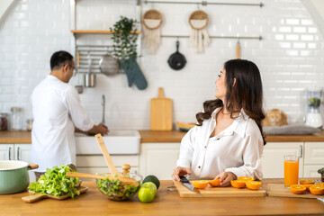 Young asian family couple having fun cooking and preparing cook vegan food healthy eat with fresh vegetable salad on counter in kitchen at home.Happy couple looking to preparing food