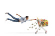 © Ljupco Smokovski - Full length shot of a casual young man flying and holding a shopping cart with food and money