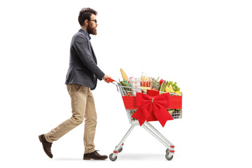 Wall Mural - Full length profile shot of a bearded guy pushing a christmas shopping cart with food products