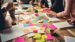 Close-up of a busy brainstorming session with multiple hands, colorful post-it notes, and documents scattered across a table, indicating a collaborative work environment.