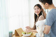 © DG PhotoStock - Man holding lovely cute Maltese dog to see his girlfriend making a salad in kitchen.