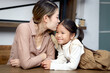© Stella - Happy family spending time at home together, Asian happy mother kissing at forehead of her cute daughter little girl child with love, lovely and happy family relationships. Parents take care of kid.