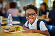 A black pupil in a school cafeteria, eating a healthy lunch together.