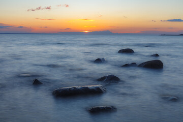 Wall Mural - Evening at the shore of Baltic sea. Bright sunset and sea waves. Erratic boulders. Long exposure.