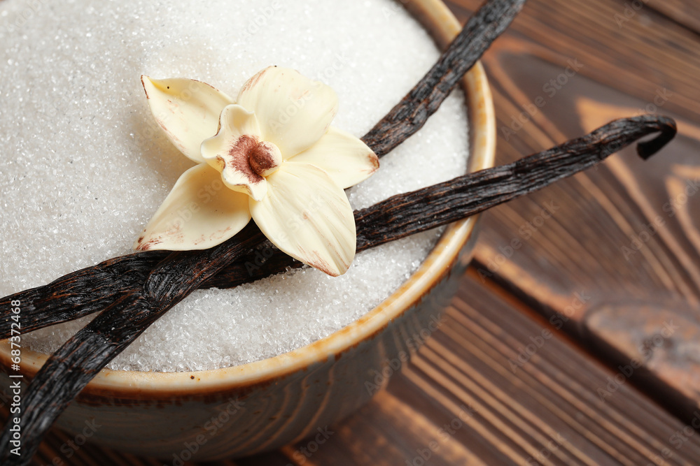 Bowl with aromatic vanilla sugar, flower and sticks on wooden background