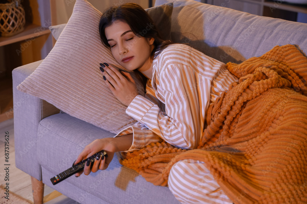 Sleeping young woman with TV remote control at home in evening