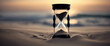  Hourglass on a beach at sunset. The hourglass is black and has white sand in it. The hourglass is on a sandy beach with the ocean in the background. The background consists of a beautiful sunset.