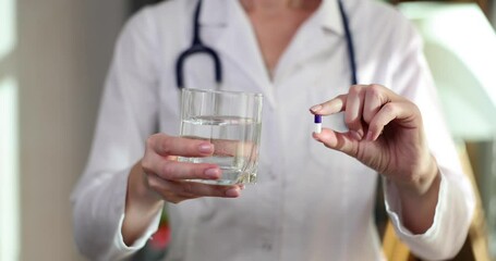 Wall Mural - Doctor holding medicine capsule and glass of water closeup 4k movie slow motion. Regular intake of medicines concept