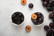 Two bowls with dried prunes and ripe raw plums on light background.Top view.