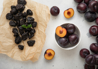 Wall Mural - Bowl with ripe raw plums and dried prunes on light background.Top view.