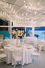 Wall Mural - Covered festive tables with bouquets of flowers on stands stand on the terrace by the sea