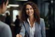 Bellissima donna manager sorridente con capelli lunghi in un moderno ufficio con abito elegante mentre stringe la mano ad un cliente
