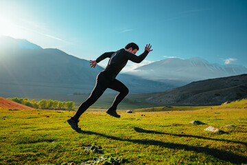 Wall Mural - Athletic young man running on mountains background at sunny day