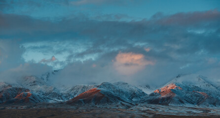 Poster - Beautiful mountain landscape with snowy peaks in overcast weather at sunset