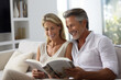 © Dzmitry - Happy elderly man and woman sitting on the sofa together and reading a book, smiling.