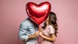 © Benjamin - couple kissing behind a red heart shaped foil balloon on pastel pink background - valentine's day - romance love concept