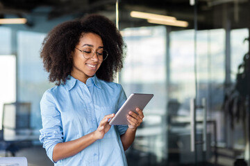 Young beautiful successful woman at workplace inside office with tablet computer in hands, female programmer testing new app, happy smiling.