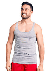 Wall Mural - Young handsome man wearing swimwear and sleeveless t-shirt looking away to side with smile on face, natural expression. laughing confident.