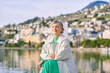 Outdoor portrait of happy mature 50 - 55 year old woman, enjoying nice spring day by the lakeside, wearing grey coat
