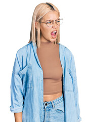 Canvas Print - Beautiful young blonde woman wearing glasses angry and mad screaming frustrated and furious, shouting with anger. rage and aggressive concept.