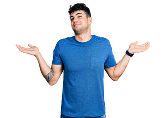 Wall Mural - Young hispanic man wearing casual t shirt clueless and confused expression with arms and hands raised. doubt concept.