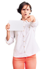 Sticker - Beautiful young woman with short hair holding blank empty banner pointing with finger to the camera and to you, confident gesture looking serious