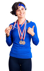 Wall Mural - Beautiful young woman with short hair wearing winner medals smiling happy and positive, thumb up doing excellent and approval sign