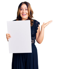 Young beautiful caucasian woman holding cardboard banner with blank space celebrating victory with happy smile and winner expression with raised hands