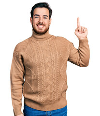 Wall Mural - Young hispanic man wearing casual clothes showing and pointing up with finger number one while smiling confident and happy.