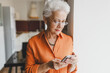 © shurkin_son - Indoor image of senior woman in glasses and casual clothes using smartphone, reading message or news, browsing social media, chatting online, texting sms, checking weather in application